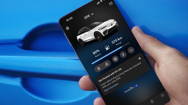 Closeup of hand holding a smartphone in front the door handle on a blue Acura. On the smartphone’s screen is an Acura with its headlights on and a line of copy that reads: “Acura. Drive like never before.”