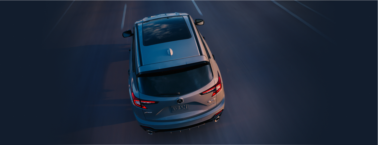 Plan de trois quarts arrière en plongée d’un RDX gris roulant sur l’autoroute à la tombée de la nuit.