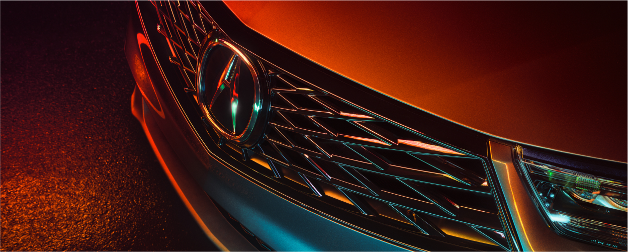 Vue à vol d'oiseau de 3/4, gros plan de la calandre avant du RDX gris la nuit, éclairée par des néons.