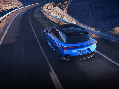 Vue 3/4 arrière à vol d'oiseau d'un ZDX bleu roulant sur une route désertique au crépuscule.