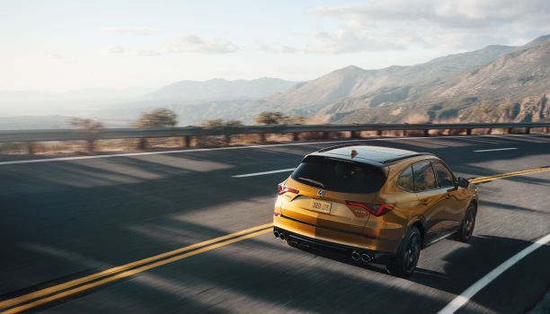 Plan étendu de trois quarts arrière d’un MDX Type S effectuant un virage sur une autoroute de montagne dans la lumière de fin d’après-midi.