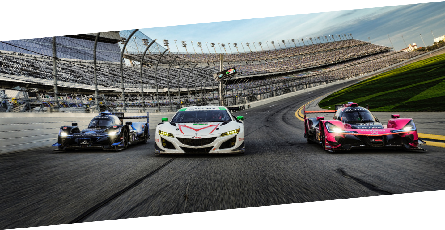 Front shot of a white Acura NSX GT3 flanked by a blue and a white Acura ARX on either side. The three cars are racing around a speedway with the stadium seating seen in the background. Vue avant d’une Acura NSX GT3 blanche entre une Acura ARX bleue et une Acura ARX rouge. Les trois voitures participent à une course sur un circuit ovale avec les estrades en arrière-plan.